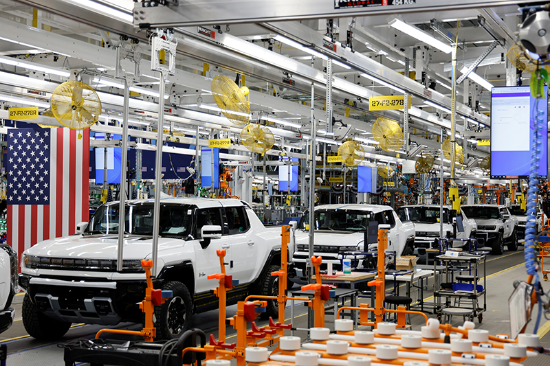 A line of nearly assembled white electric trucks passes through a factory.