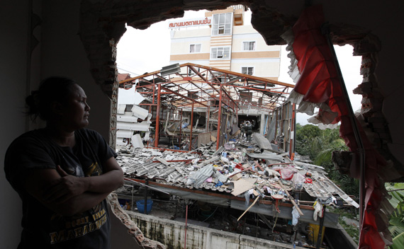 A local resident watches from inside his damaged house as investigators inspect the site of a bombing in the suburbs of Bangkok