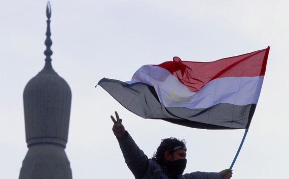 An opposition supporter flashes the victory sign as he holds an Egyptian flag atop a lamp post near a mosque in Tahrir Square in Cairo