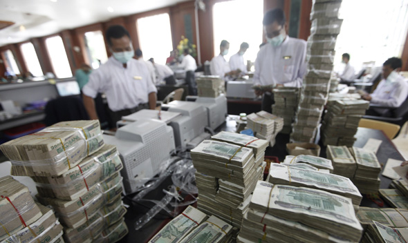 Cashiers are seen behind piles of kyat banknotes as they count it in a private bank in Yangon July 21, 2011.