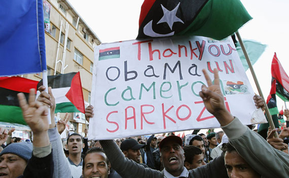 A protester holds a banner beneath a Kingdom of Libya flag during an anti-Gaddafi demonstration in Benghazi on March 31, 2011.