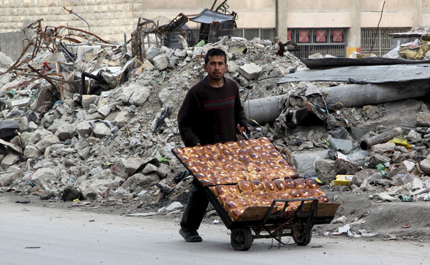 A man selling pastries walks past the rubble of damaged buildings in the rebel held al-Shaar neighborhood of Aleppo, Syria, February 10, 2016. REUTERS/Abdalrhman Ismail