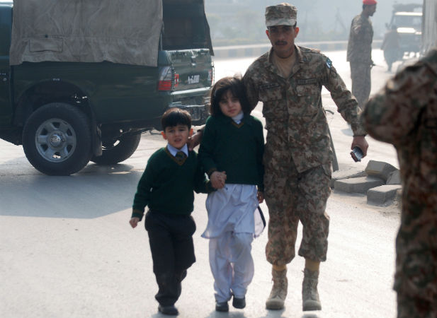 A soldier escorts schoolchildren from the Army Public School that is under attack by Taliban gunmen in Peshawar.