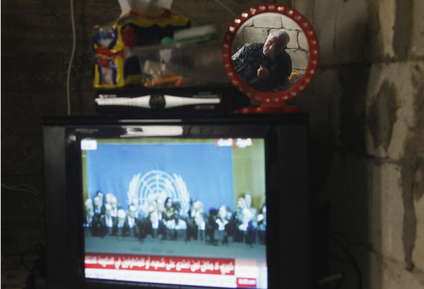 Syrian refugee reflected in a mirror as he watches the Geneva II peace conference on television at the port city of Sidon, southern Lebanon.