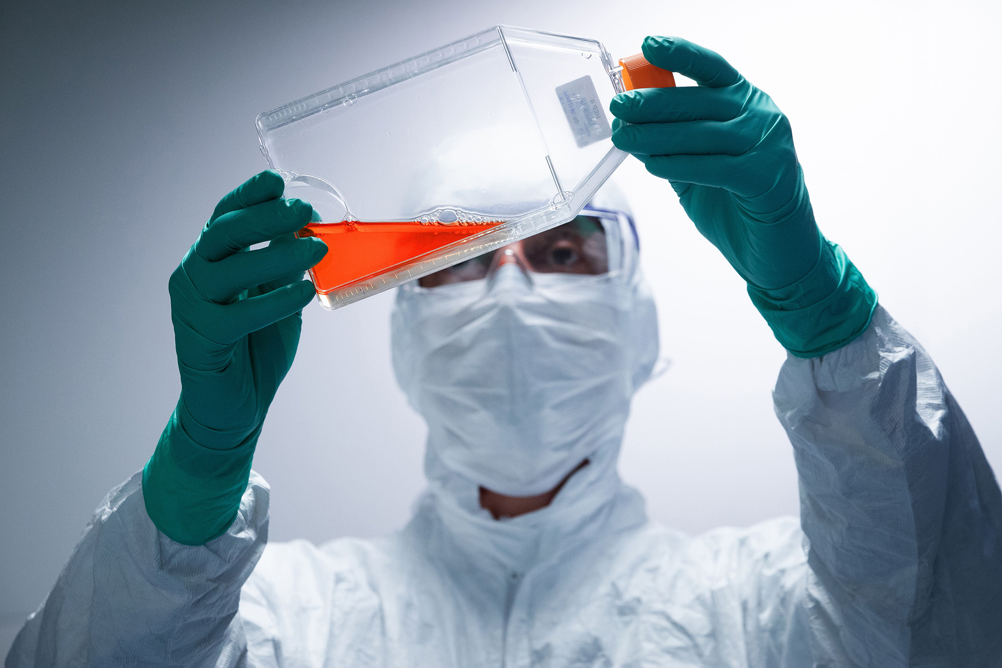 A lab technician wearing Personal Protective Equipment (PPE) looks at a bottle containing a reagent before performing vaccine test.
