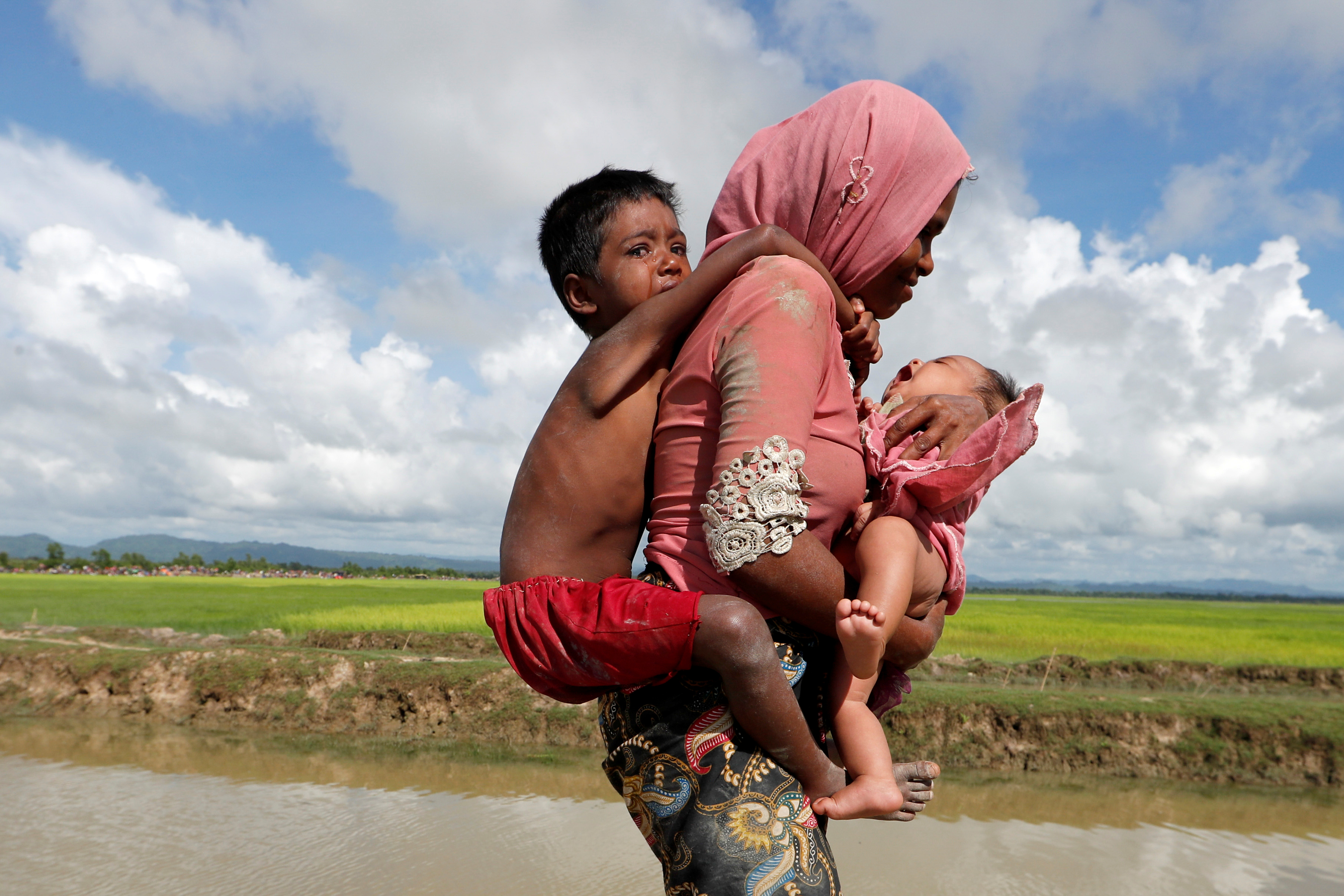 Rohingya refugees walk in a rice field 