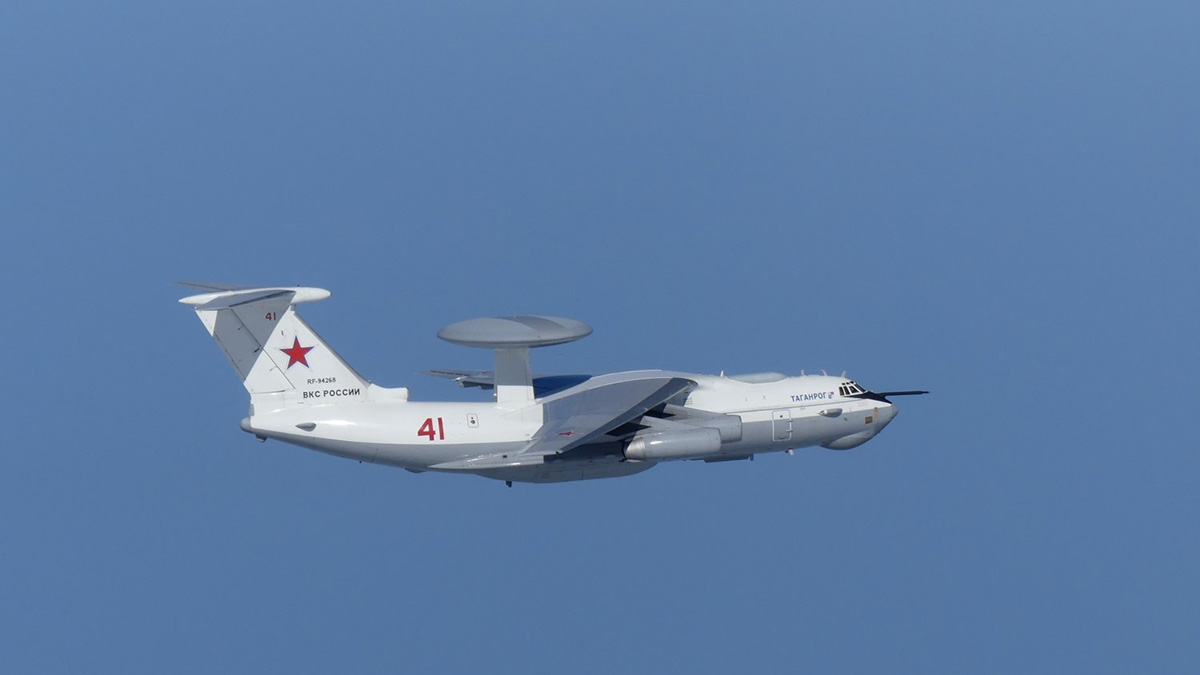 A white military plane flies in a blue sky.