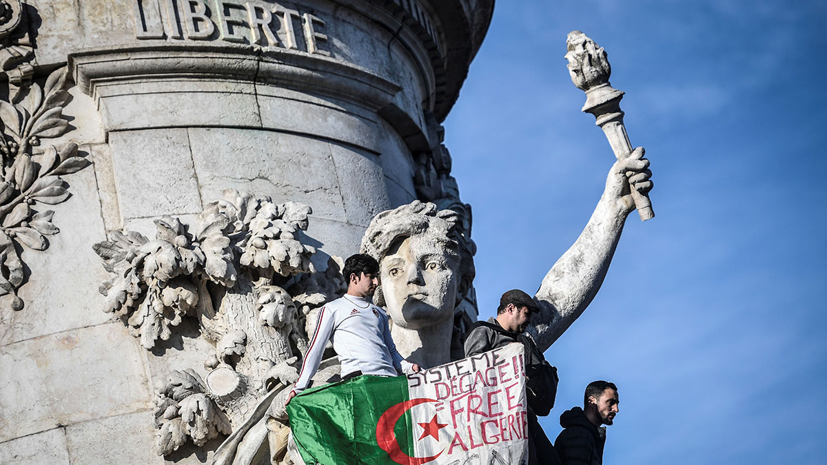 Algerian protesters in Paris hold a sign reading, “System get out, free Algeria.”