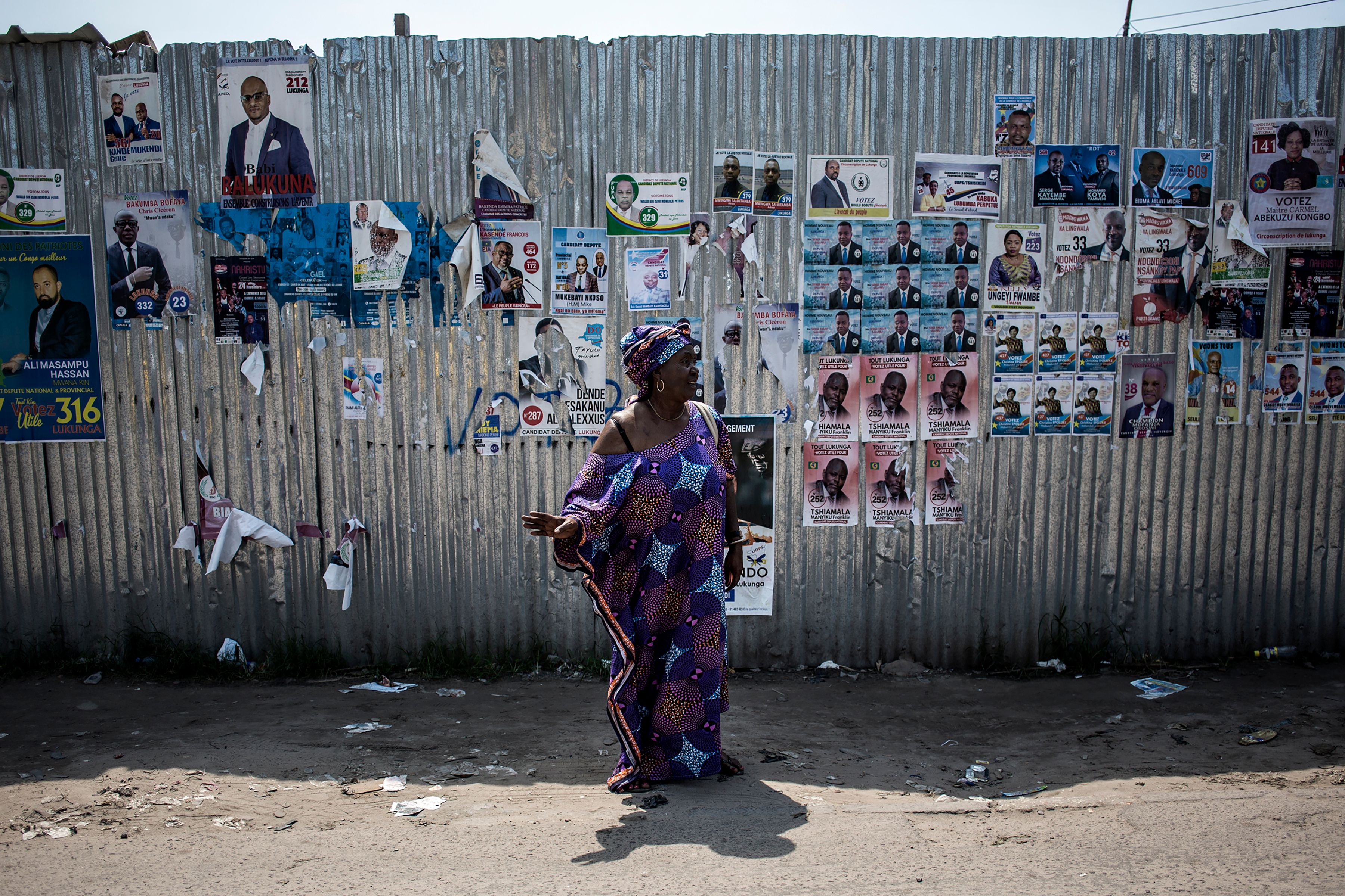 A woman signals for a taxi in front of a wall filled with campaign posters in Kinshasa.