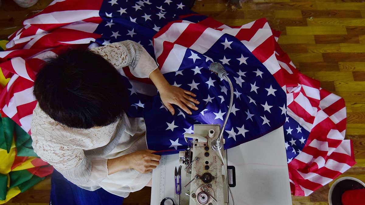 A Chinese factory worker sews an American flag