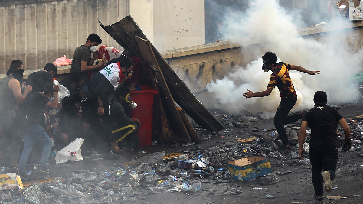 Iraqi anti-government protesters stand behind a barricade as security forces fire tear gas to keep demonstrators from storming the Green Zone, which hosts government offices and foreign offices, on October 28, 2019 in Baghdad
