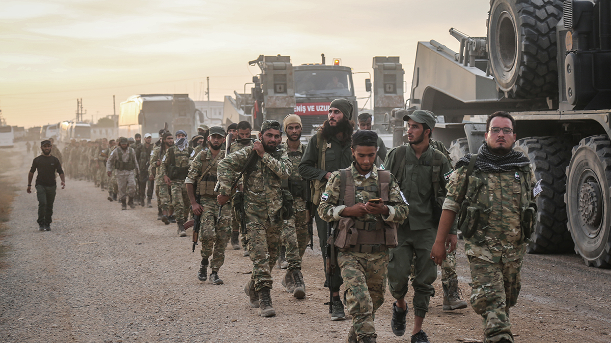 People dressed in camouflage walk in rows down a dusty street in Turkey. 