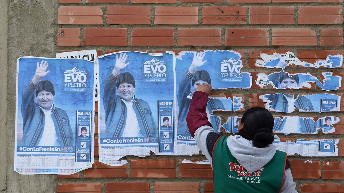 A woman removes posters of Morales from a wall.
