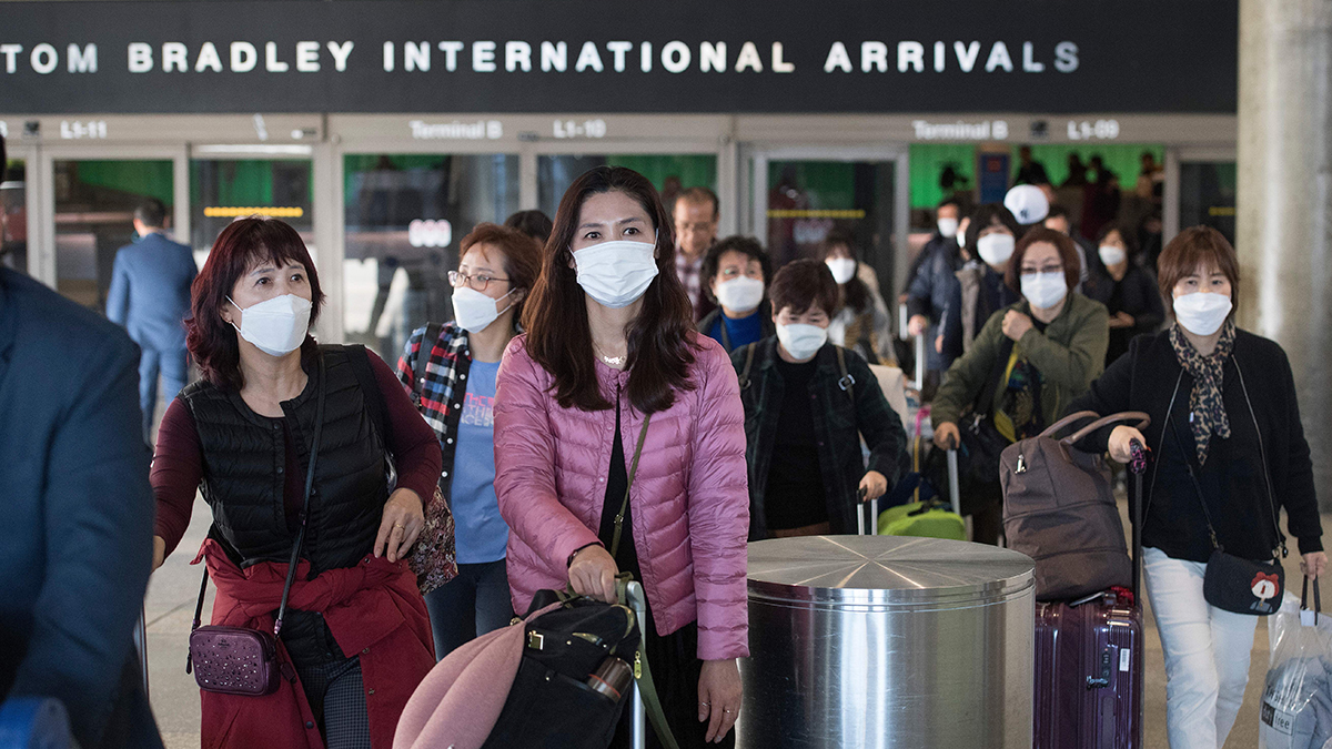 People wear masks and push luggage as they walk out of a U.S. airport.
