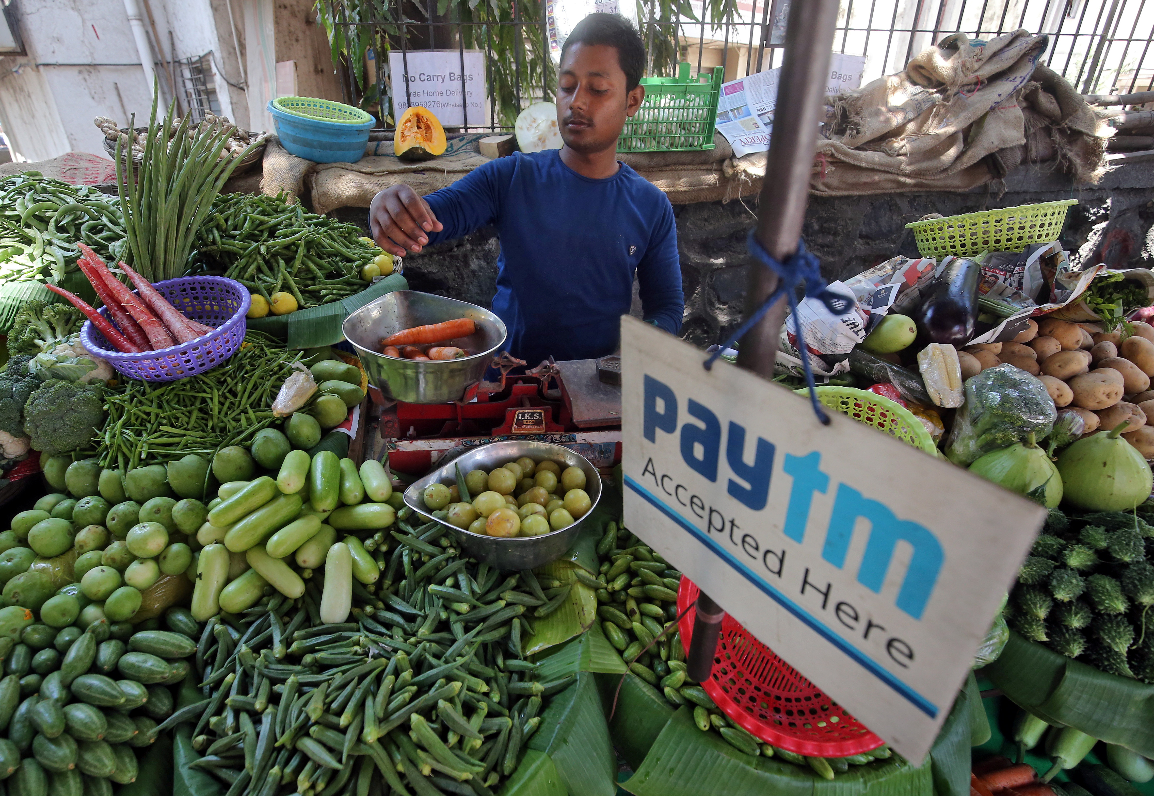 A vendor weighs vegetables next to an ad for Paytm, a digital payments firm, at a roadside market in Mumbai.