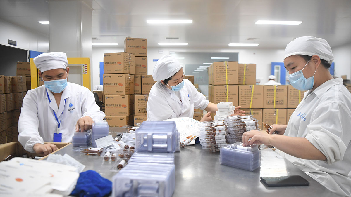 Three workers in a Chinese pharmaceutical factory pack medicines into plastic containers. 