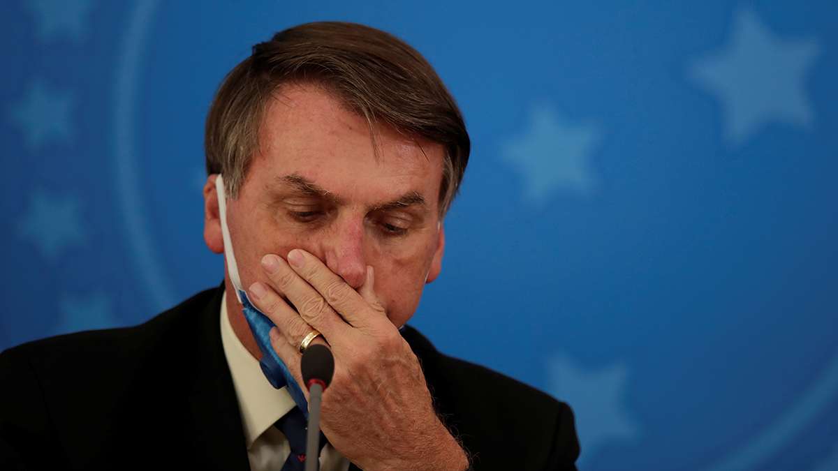 Brazilian President Jair Bolsonaro holds his hand over his mouth as he wears a protective mask during a news conference.