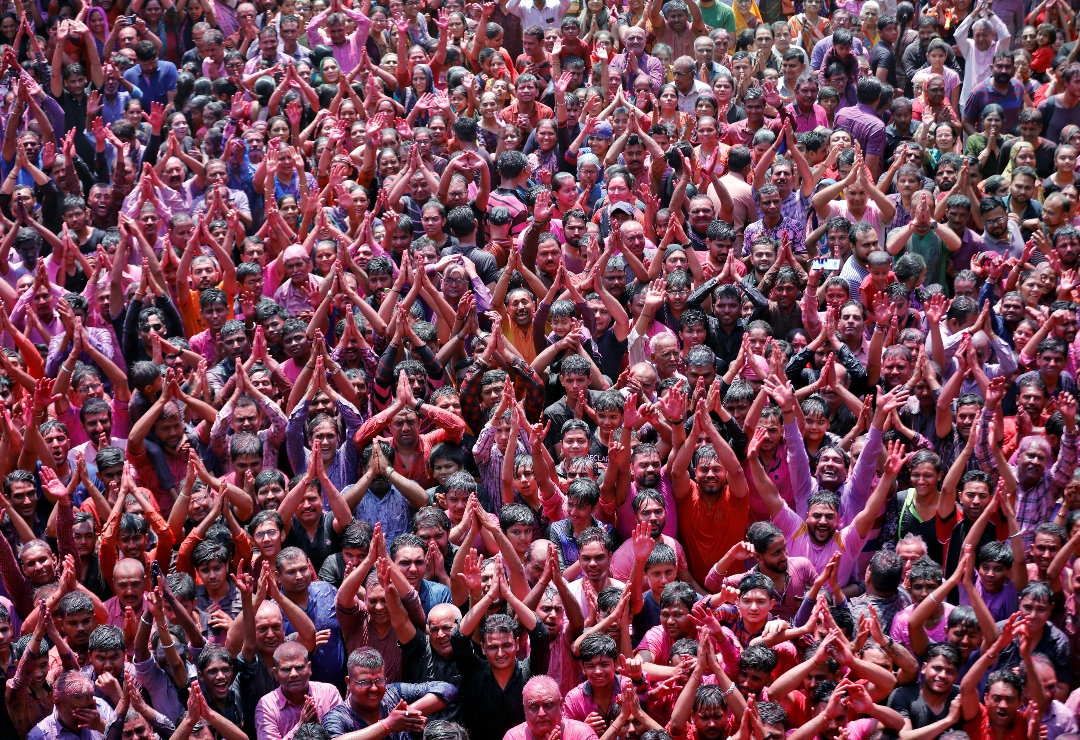 A crowd of Hindu devotees covered in multicolored dye raise their hands above their heads in prayer.