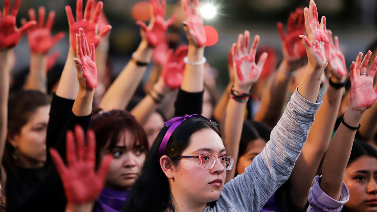 A group of Mexican women raise their hands, which are painted red, during a protest against gender-based violence.