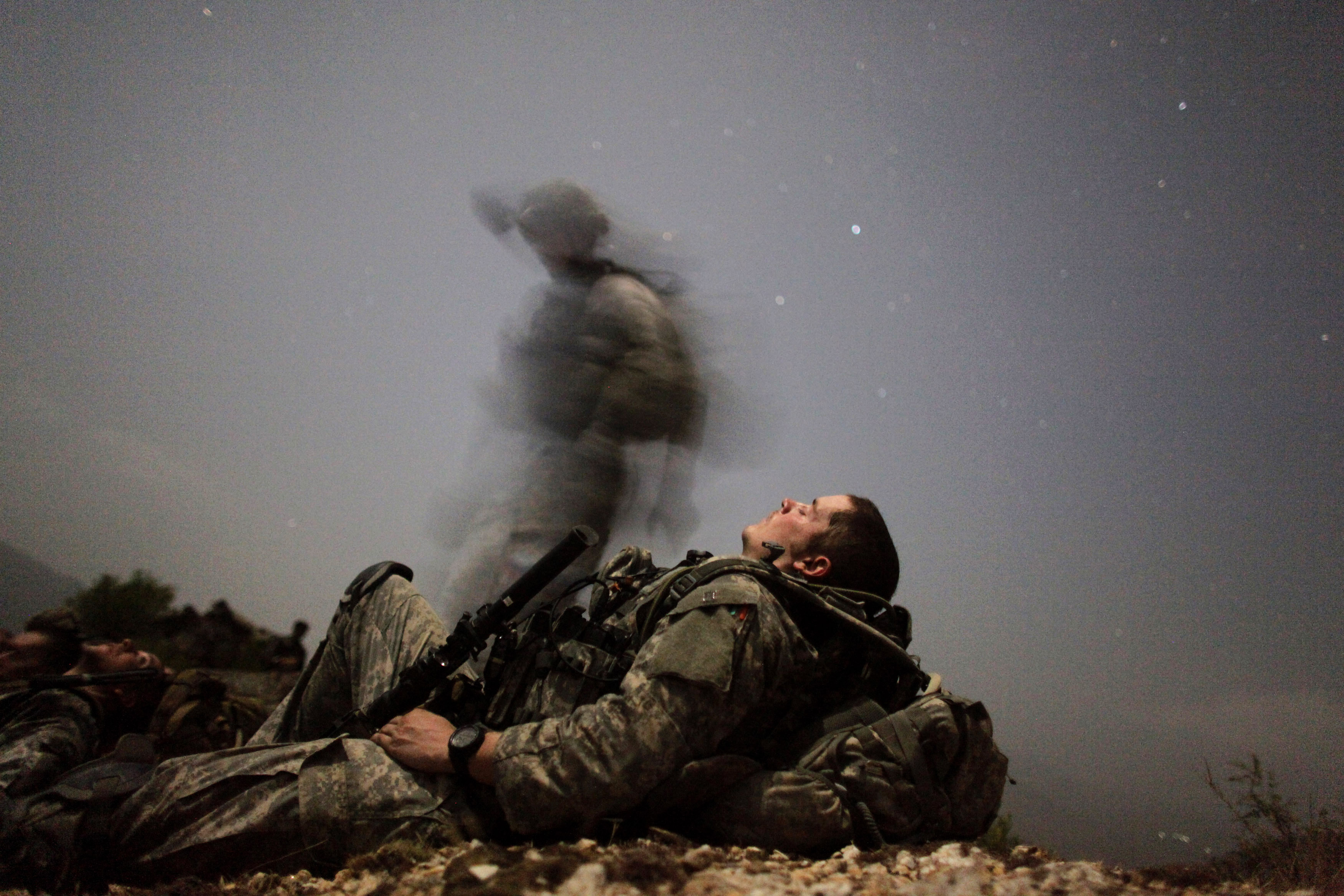 A U.S. soldier of 2-12 Infantry 4BCT-4ID Task Force Mountain Warrior takes a break while another soldier walks by, out of the camera's focus, during a night mission near Honaker Miracle camp at the Pesh valley of Kunar Province, August 12, 2009.