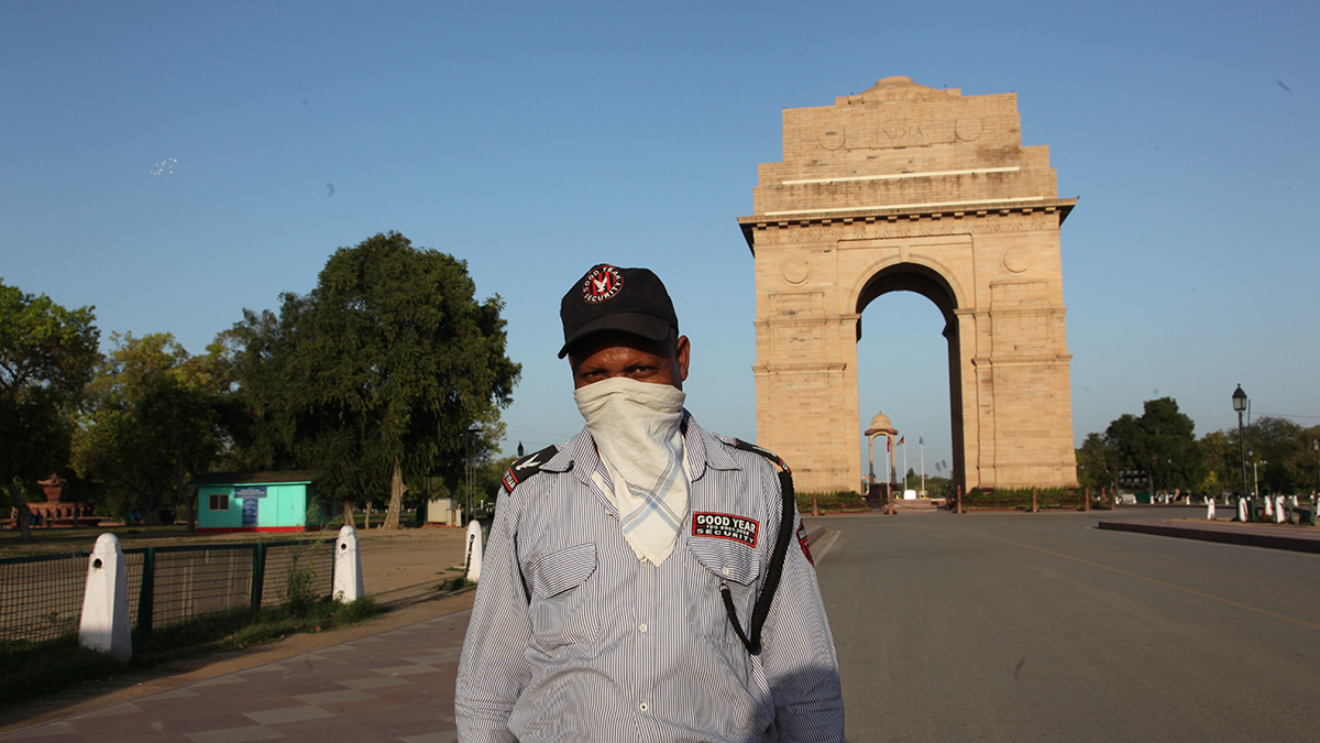 A man wears a face mask in front of New Delhi's India Gate, seen with blue skies. 