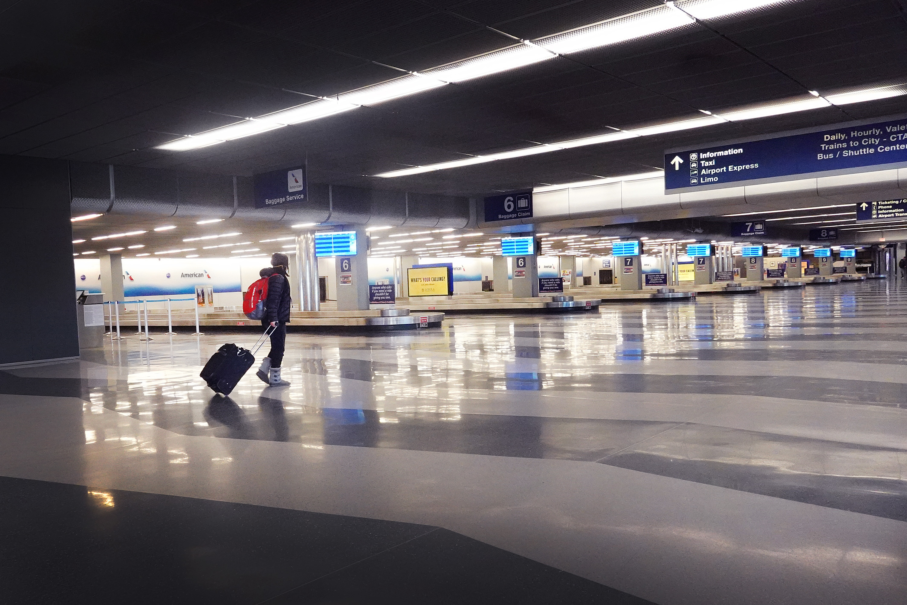 A person pulls a suitcase through a nearly empty airport baggage claim area.