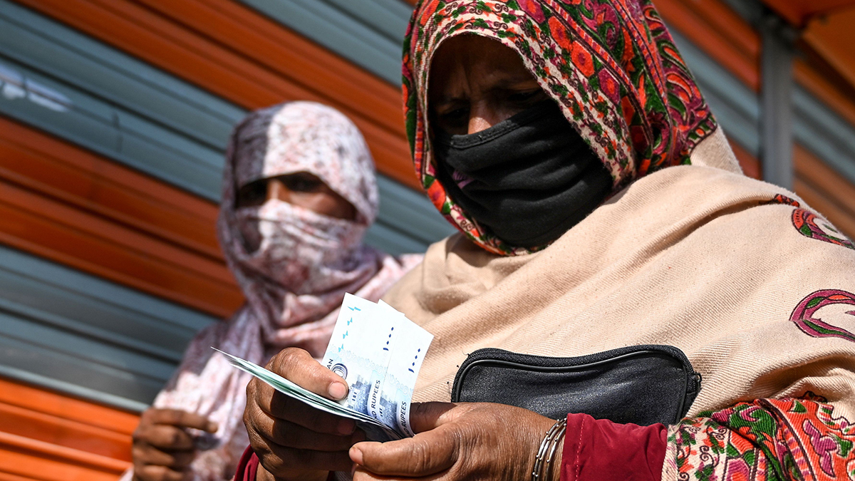 A woman wearing a mask and colorful head scarf counts money. 