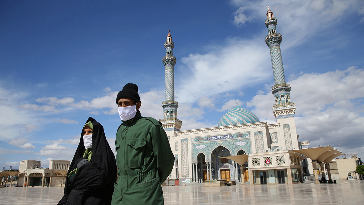 A man and woman wearing surgical masks walk in front of a mosque amid a coronavirus outbreak in Qom, Iran.