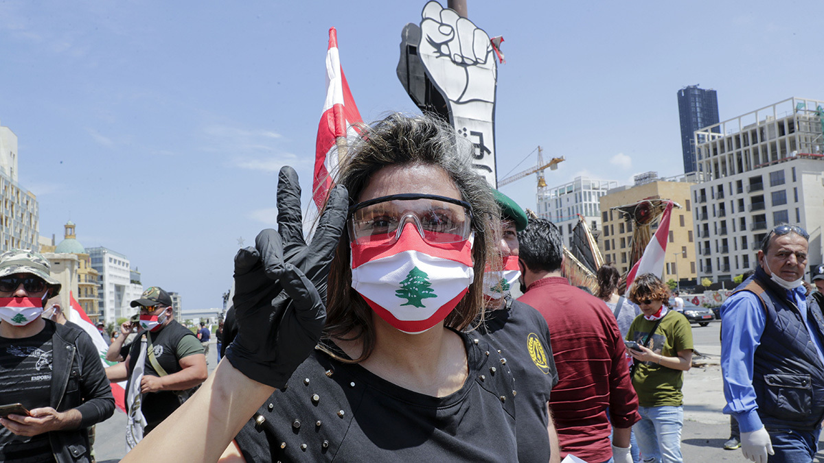A woman wearing a face mask resembling Lebanon's flags hold her hand in a peace sign during Beirut protest.
