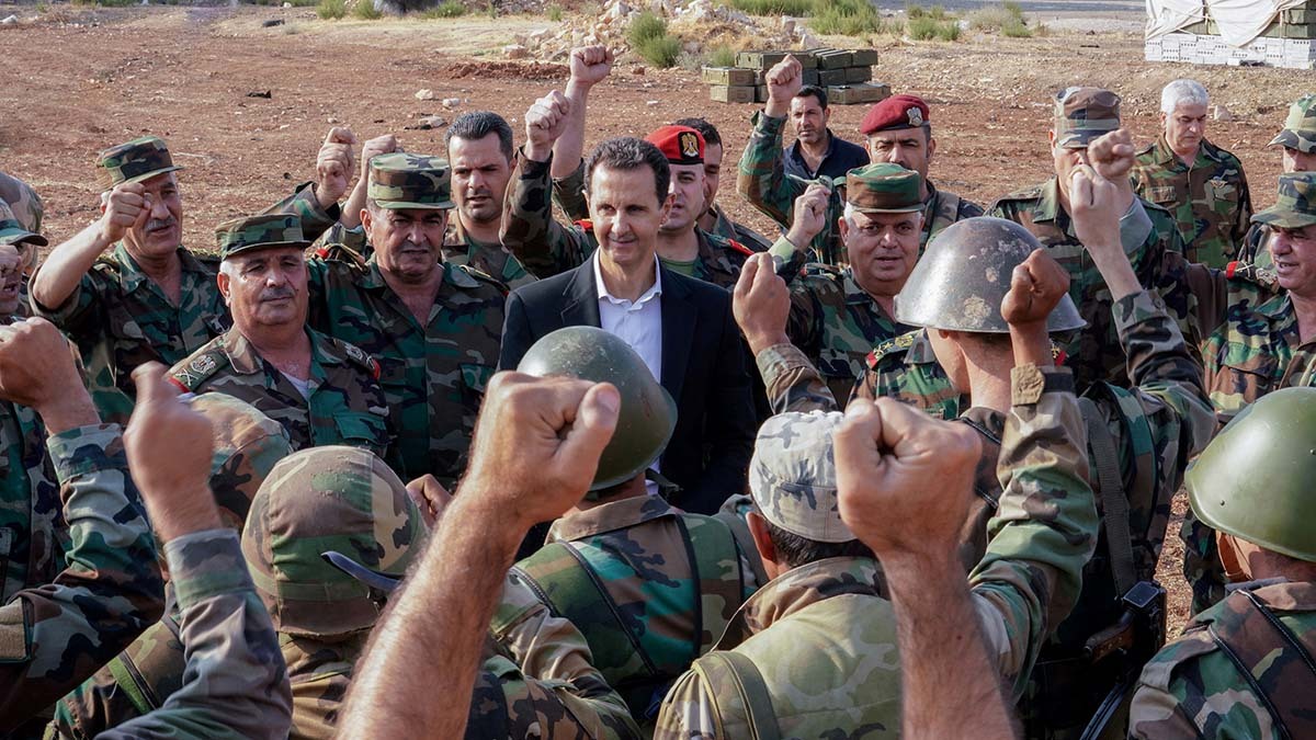 Syrian President Bashar al-Assad stands in the middle of a group of soldiers who are facing him and raising their fists
