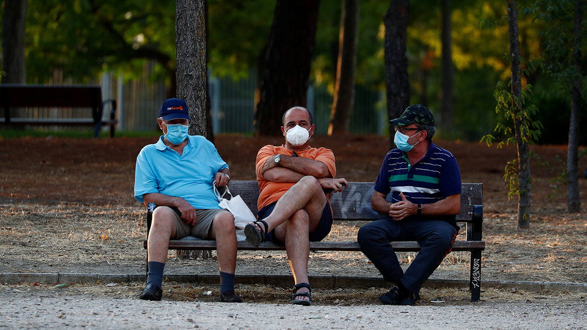 Three men wearing protective face masks sit on a bench at Las Cruces Park in Madrid, Spain, amid the coronavirus pandemic, July 28, 2020.