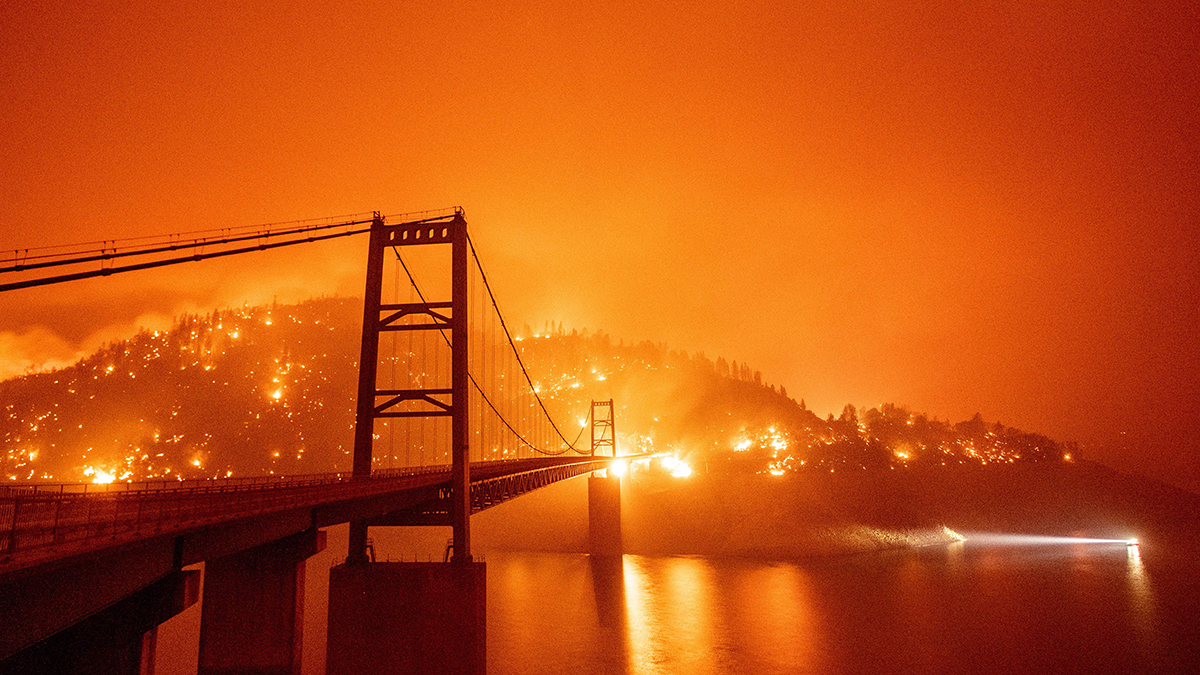 Fires are seen on a ridge near a bridge in California. The sky is orange.
