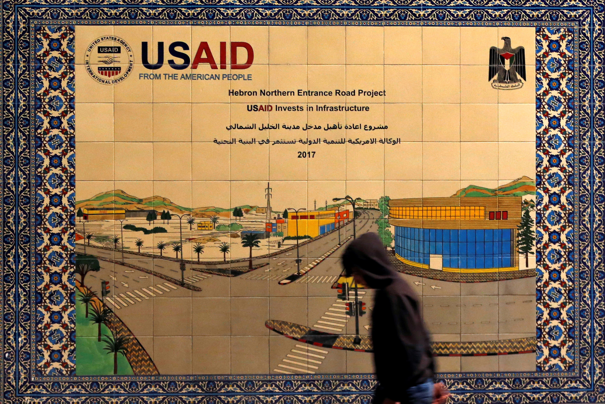 A Palestinian walks past a ceramic sign of a U.S. Agency for International Development (USAID) project in Hebron in the Israeli-occupied West Bank