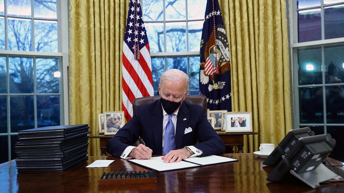 Biden signs a document in the Oval Office of the White House.
