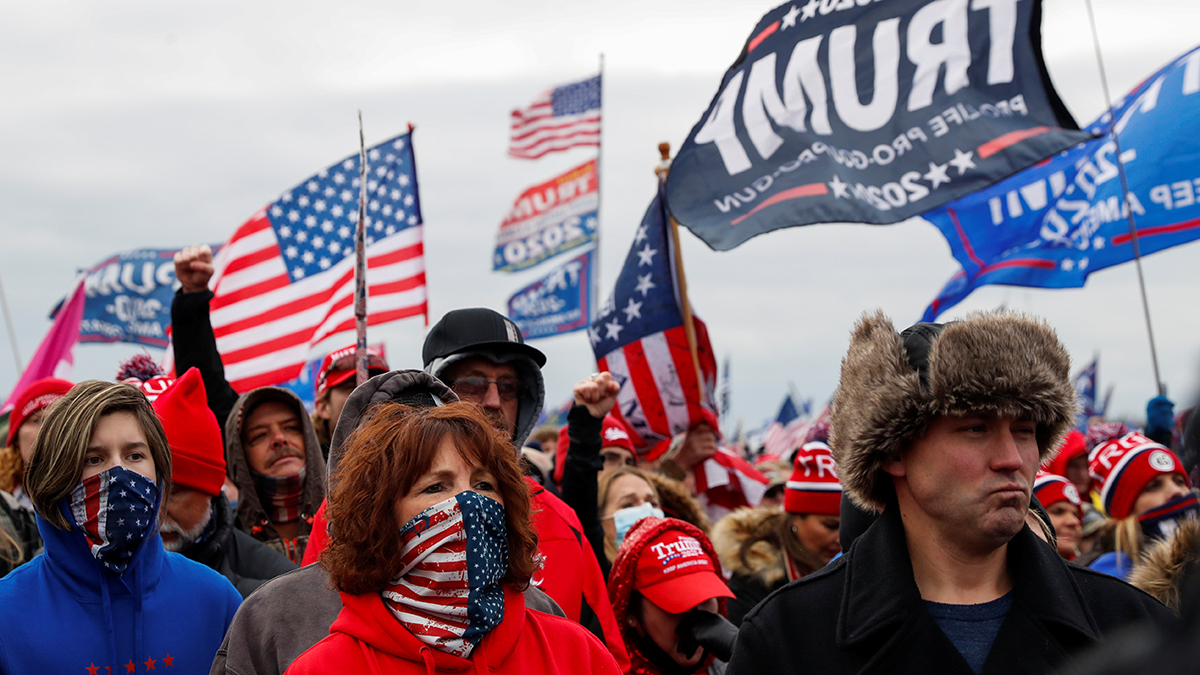 A crowd of people are shown holding American flags and flags with President Trump's name on them