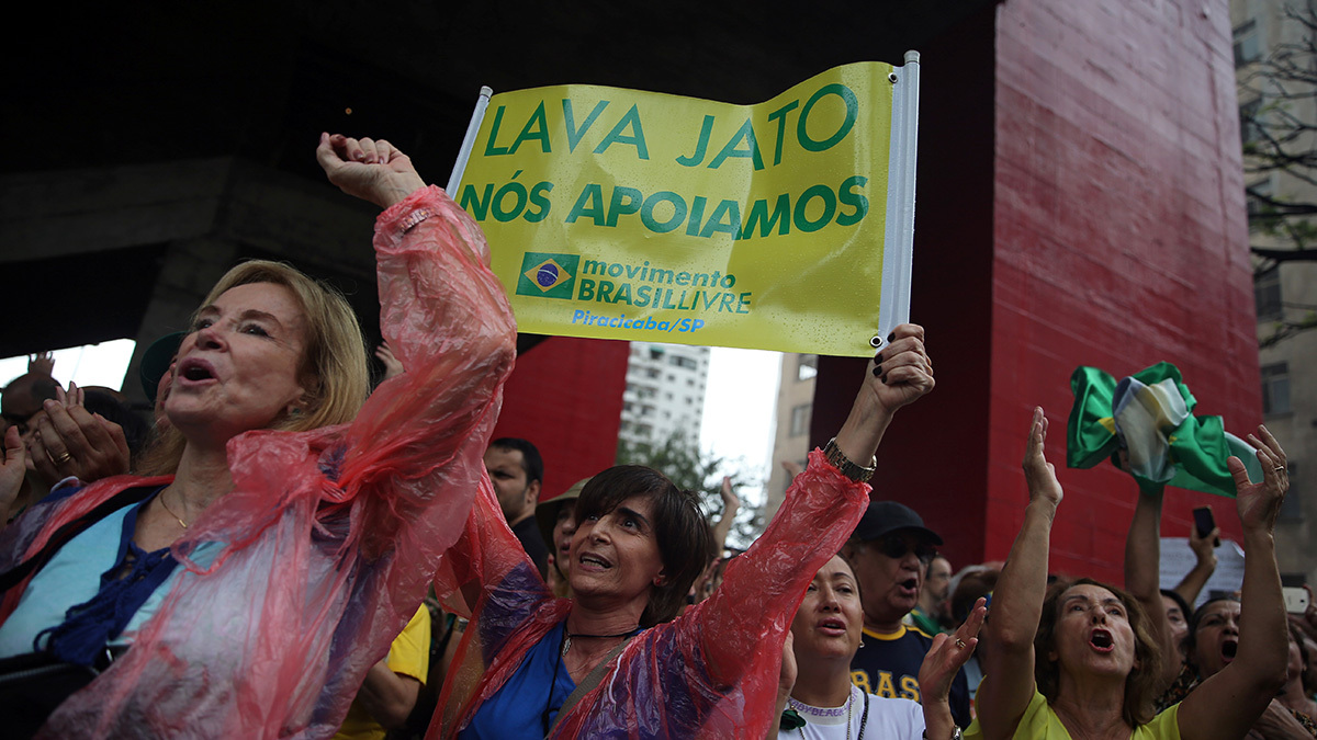 A group of people, several with their arms raised.  One woman is holding a yellow and green sign above her head.