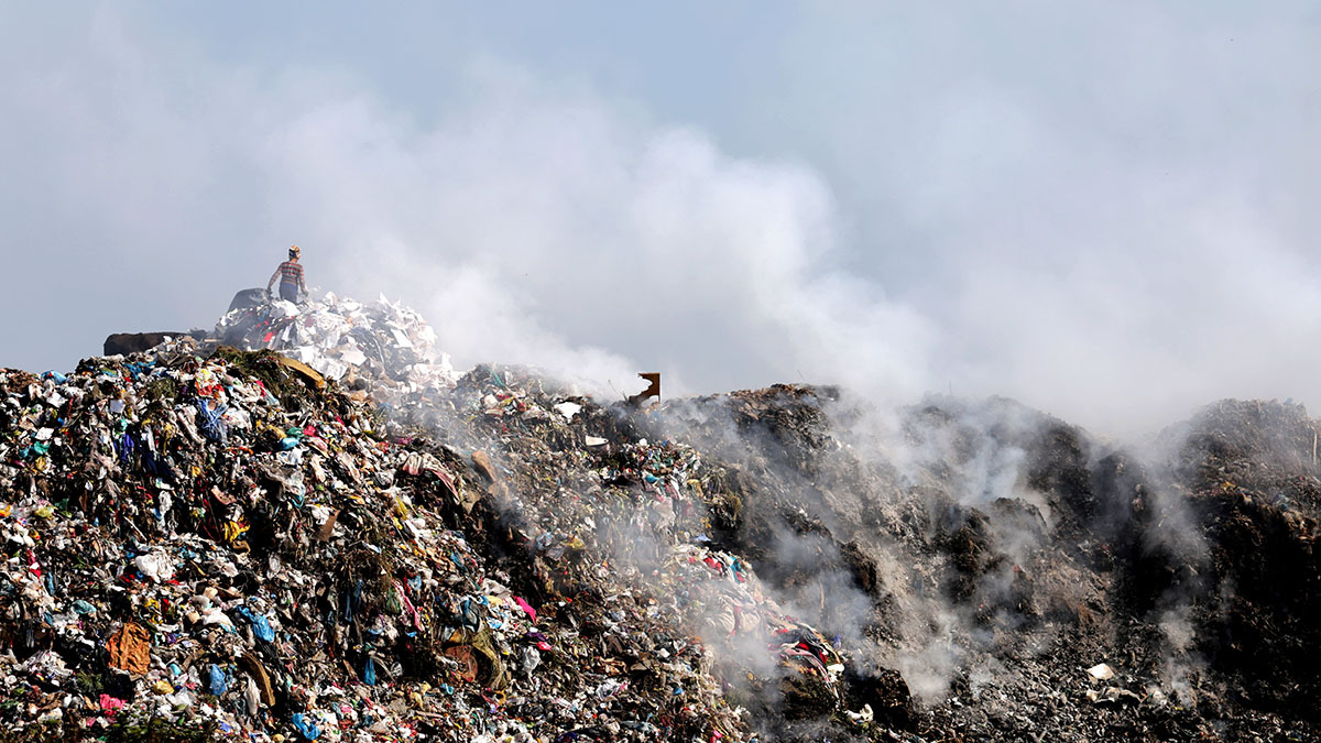 Smoke rises from a landfill full of waste.