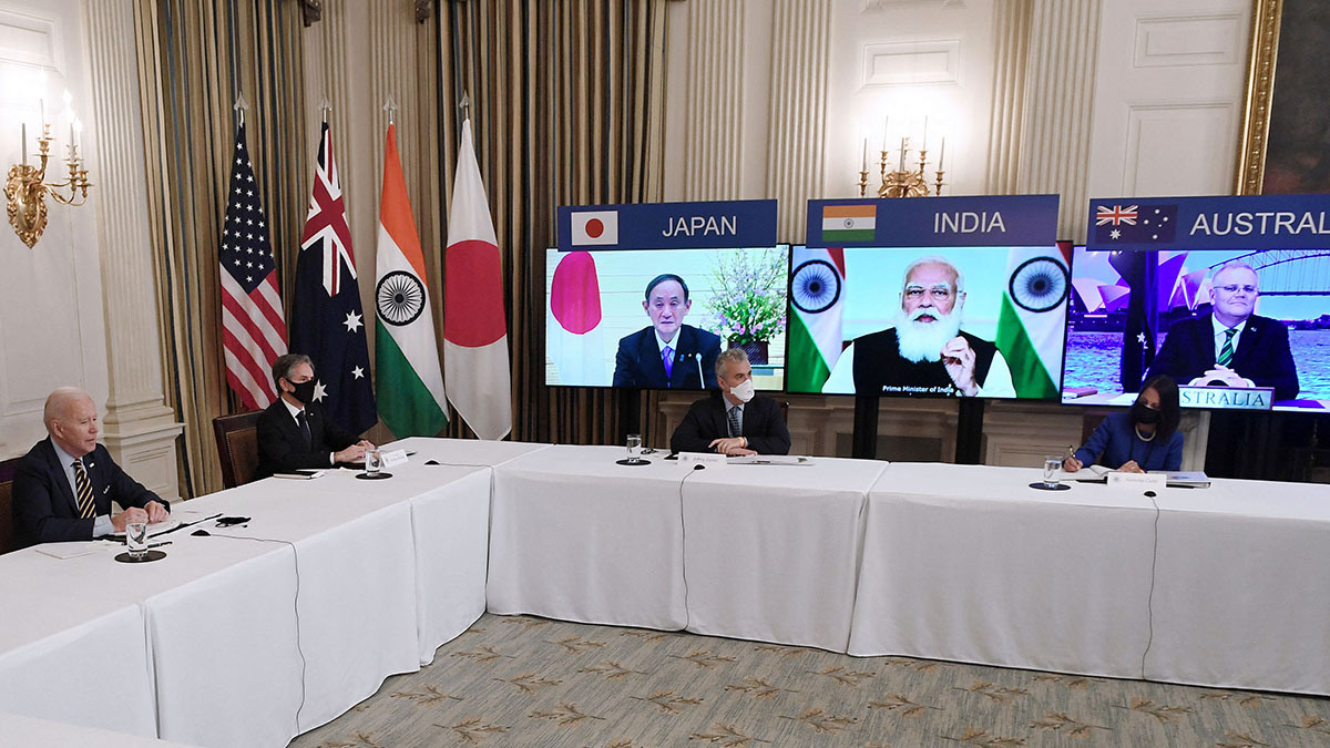 President Biden sits at a table and the leaders of Japan, India, and Australia appear on video screens.