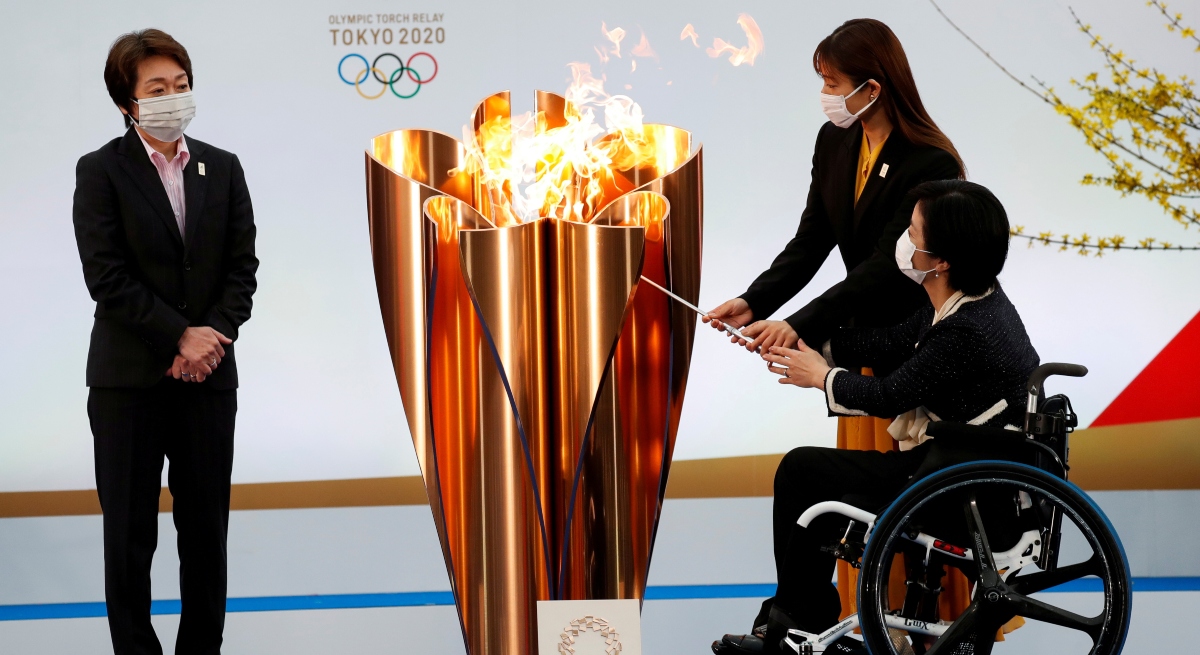 Seiko Hashimoto stands left of Olympic cauldron lit by actor Satomi Ishihara and athlete Aki Taguchi, who is in a wheelchair.