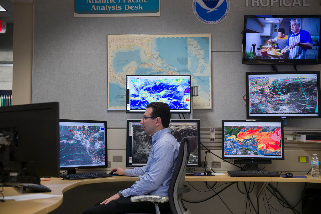 A meteorologist works at his desk with multiple monitors showing different weather forecasting tools at the National Hurricane Center in Miami, Florida.