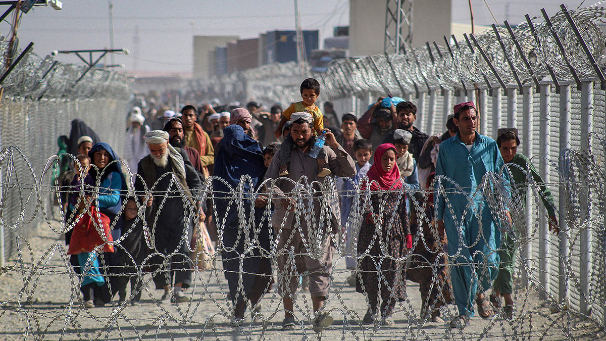 A group of Afghans walk between fences covered in barbed wire at a Afghanistan-Pakistan border crossing.