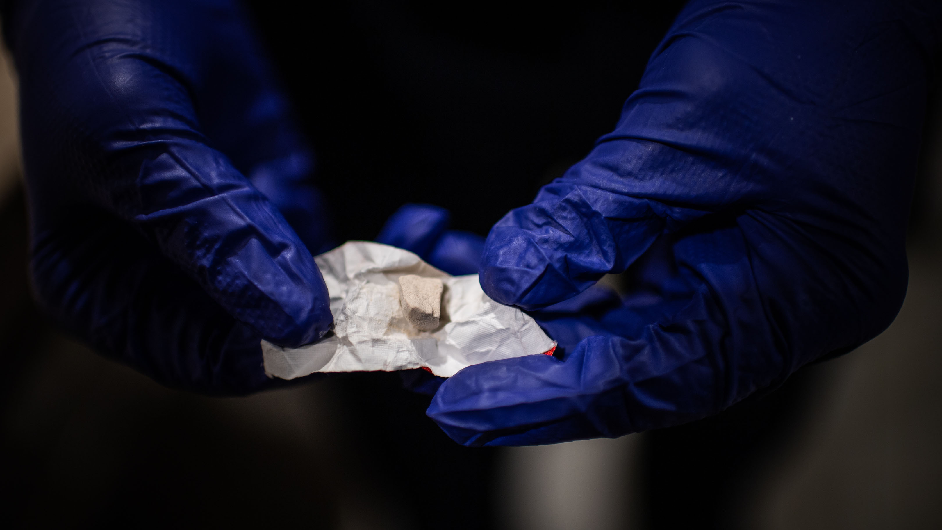 A close-up of a police officer wearing gloves holding a small amount of heroin and fentanyl wrapped in a piece of paper.