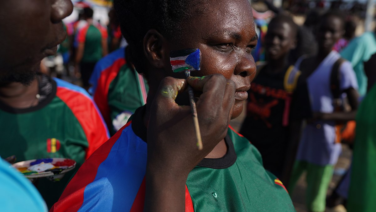 An artist is painting a South Sudan flag on a woman's cheek, after The Great South Sudan Run, at John Garang Mausoleum, during the country's 10th anniversary since independence, on July 9, 2021 in Juba, South Sudan. 