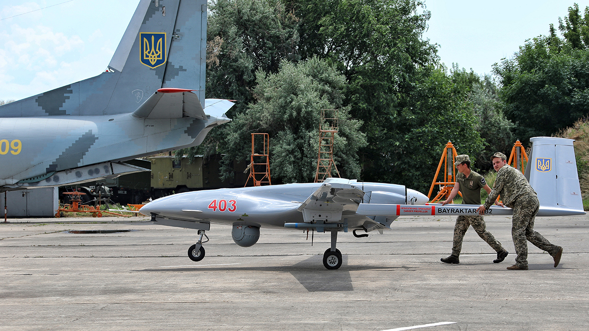 Soldiers push a drone on the tarmac.