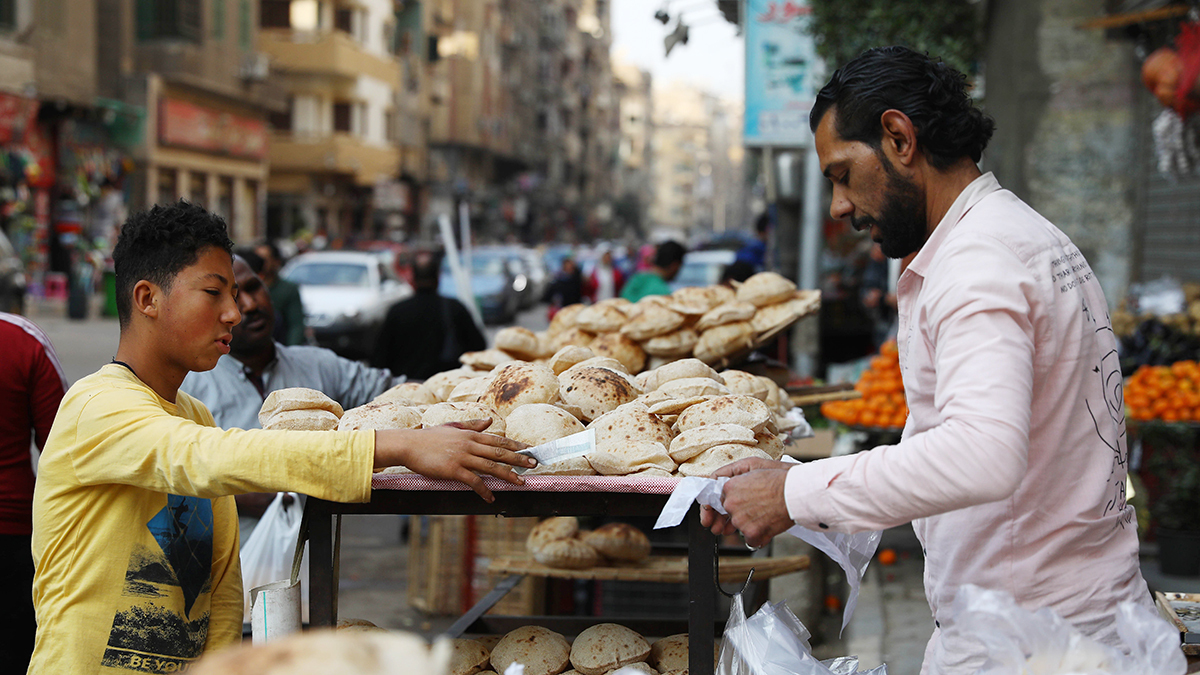 A boy hands money to a man selling bread at an outdoor market in Cairo