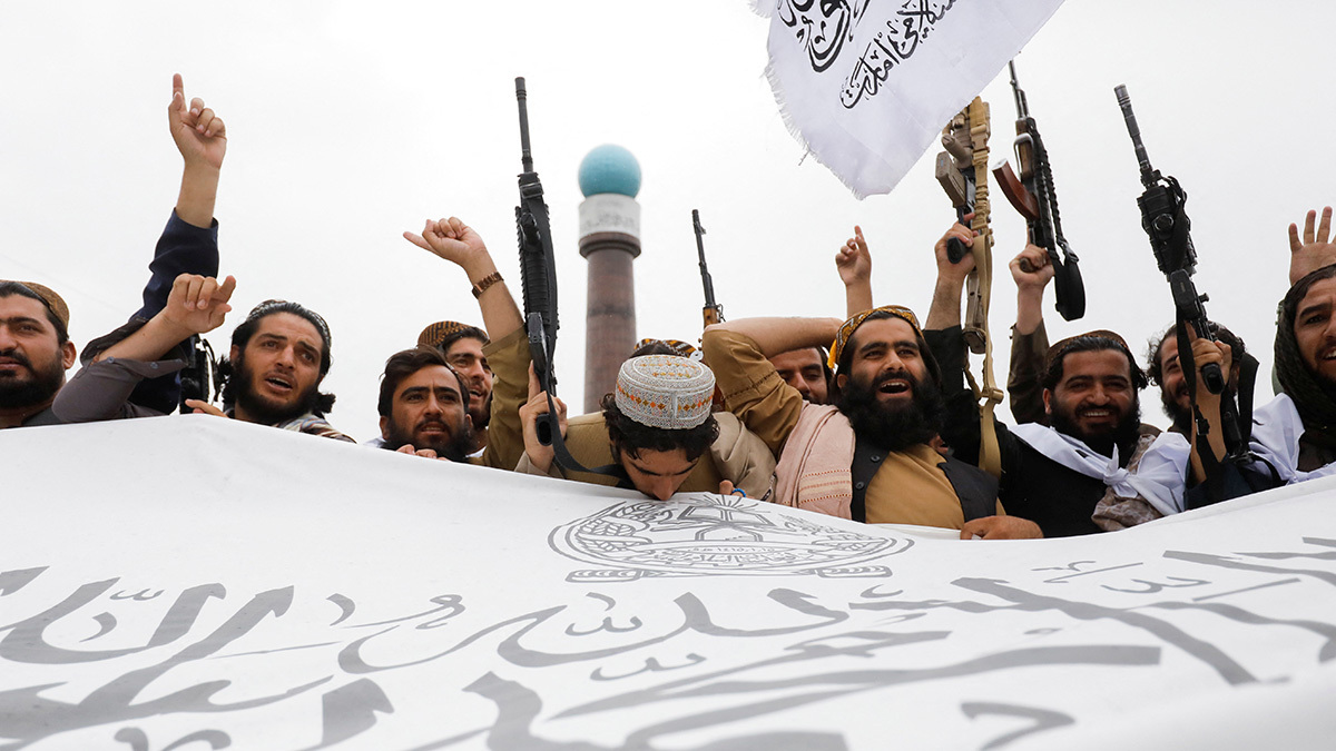 Taliban fighters cheer and hold a flag for the Islamic Emirate of Afghanistan.