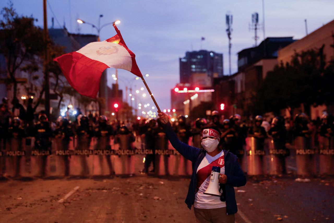A protester waves the Peruvian flag as police stand guard during nationwide protests following President Pedro Castillo Terrones’s removal.