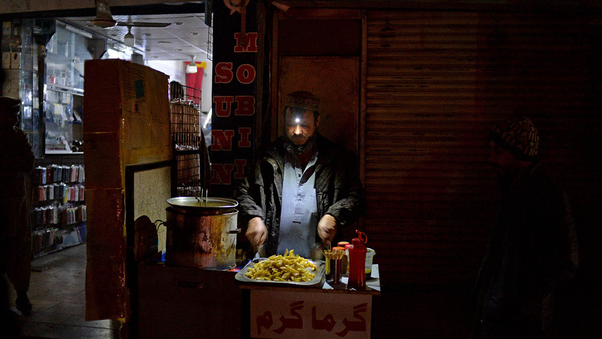 A street vendor cooks by headlamp as the darkness encroaches on the background.