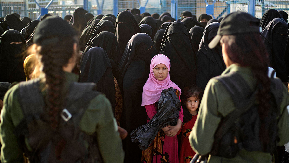 Kurdish troops seen from behind monitor a crowd of Muslim women veiled in black, as well as two young girls.