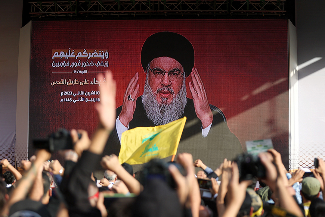 Hezbollah leader Hassan Nasrallah appears on a screen as he addresses cheering supporters, seen from behind.